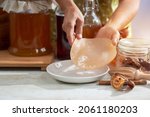 Small photo of Woman holding the Scoby or fungus over white plate, Scoby tea mushroom to start the fermentation process to make Kombucha, dietetic organic superfood healthy fermented tea