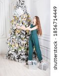 Small photo of Lass wearing in green one-piecer and black sandals stands near Christmas tree and catches a big handsel