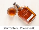 Small photo of Moscow, Russia - September 22, 2021: glass and lying bottle with Woodford Reserve straight bourbon whiskey on light table. Making fine bourbon began on the site Woodford Reserve Distillery in 1812