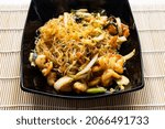 Small photo of portion of Mien Xao Vietnamese wok stir-fried glass noodles with vegatables and prawns in black bowl close up on wooden table