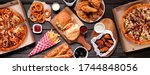 Small photo of Table scene of assorted take out or delivery foods. Hamburgers, pizza, fried chicken and sides. Top down view on a dark wood banner background.