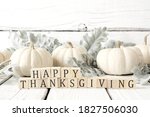Happy Thanksgiving greeting on wooden blocks against a white wood background with white pumpkins and autumn leaves