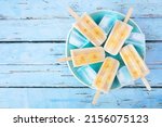 Healthy banana yogurt ice pops. Top down view over a rustic blue background.