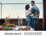 Romantic evening. Back view of young couple in casual clothes are looking at each other while standing on rooftop terrace