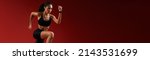 Small photo of Higher and higher. Full length of young athlete woman in sports clothing jumping against red background