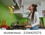 Smiling happy young female with braids opens kitchen cabinet, woman cooking at home