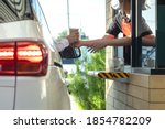 Hand of customers in the car is picking up a personal cup of coffee from the salesman  wearing a mask to prevent the coronavirus outbreak by driving through or drive thru. (Social distancing)