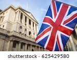 British Union Jack flag flying in front of the traditional architecture of the Bank of England in the financial center of the old city of London, UK