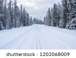 Snowy Forest Road in the Canadian Rockies on a Winter Day. A Car on the Road is Visible in Distance. Concept of Dangerous Driving Conditions.