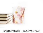 Closeup of jar filled with money papers near stack of books, isolated in white background
