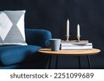 interior and home decor concept - close up of blue chair with pillow, candles, books and mug on coffee table in dark room