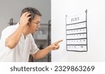 Small photo of Confused Asian Senior Man With Dementia Looking At Wall Calendar