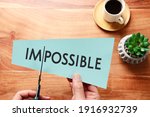 Small photo of man hand holding card with the text impossible, cutting the word im so it written possible. success and challenge concept.