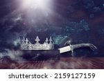 low key image of beautiful queen or king crown over antique book next to sword. fantasy medieval period. Selective focus