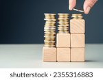 Small photo of Hand add a few coins at the top of the final level built by wood cubes as step stairs, paying less at the long term, reduce cost, save for future, insurance, and investment, or subsidy money concept