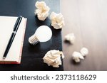 Original idea for writing, closeup light bulb with notebook and crushed paper balls on the desk, and some trash on the ground