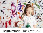 Cute child with smuges of colorful paint showing a paint brush. Little artist.