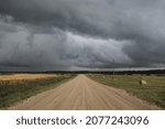 Small photo of An empty country road through the agricultural fields and forest during the storm. Dramatic sky, dark clouds. Nature, vacations, freedom, remote places, dangerous driving, fickle weather concepts