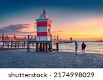Small photo of Tourists on the shore of Lignano Sabbiadoro resort. Splendid outdoor scene of Adriatic coast of Italy with lighthous and old wooden pier. Picturesque morning seascape of Mediterranean sea.