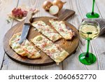 Small photo of Typical tarte flambee from Alsace with sour cream, onions and smoked bacon hot from the oven, served with Alsatian white wine