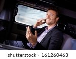 Handsome young businessman traveling in limousine, working on laptop computer, talking on mobile phone, smiling.