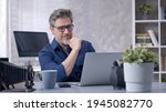 Small photo of Bearded man working online with laptop computer at home sitting at desk. Businessman in home office, browsing internet. Portrait of mature age, middle age, mid adult man in 50s.
