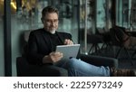 Small photo of Businessman using tablet computer in office lobby or on cafe terrace. Happy middle aged man, entrepreneur, small business owner working online.
