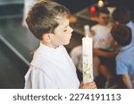 Small photo of Little kid boy receiving his first holy communion. Happy child holding Christening candle. Tradition in catholic curch. Kid in a white traditional gown in a church near altar.