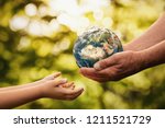 Close up of senior hands giving small planet earth to a child over defocused green background with copy space 