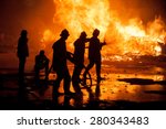 Small photo of Silhouette of Firemen fighting a raging fire with huge flames of burning timber