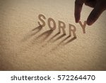 SORRY wood word on compressed or corkboard with human's finger at Y letter.