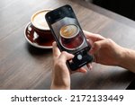 Small photo of BANGKOK, THAILAND- 25th June 2022 : Hands woman using Iphone 13pro taking photo of a cup of latte in cafe for post in social media