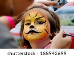 Young girl (female age 4-5) getting her face painted like a lion by a face painting make up artist on Halloween or Purim carnival Jewish holiday. Real people. Copy space