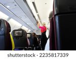 Small photo of BRISBANE - OCT 31 2022: Qantas airways female flight attendant closing the overhead luggage compartment lid for carry on baggage before take off.In Australia 1 flight attendant for every 36 passengers