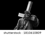 Jesus Christ with cross.  Ancient statue isolated on black background. 
