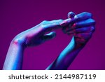 Small photo of Photo of graceful thin hands with sparkling silvery skin in bright neon blue and pink lighting. Body painting, body art. Glitter makeup. Beauty industry, cosmetology.