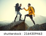 Small photo of One tourist climber helps another, standing on top of a mountain. Friendship and mutual assistance. Extreme sports, mountain tourism.