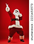 Small photo of Full length shot of Santa Claus in sunglasses listening to music on headphones, singing and dancing. Merry Christmas. Party. Red background.