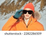 Winter sport in the mountains. Portrait of a fashionable girl posing in orange ski suit against a snowy winter landscape. Winter fashion. 