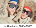 Portrait of two fashion model girls posing in white downy overalls against outdoors. Alpine skiing, active winter recreation. Winter fashion.