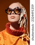 Small photo of Fashion model girl posing in stylish diamond-shaped glasses and an orange top on a studio background. Fashion and style for sunglasses. Summer haute couture collection.