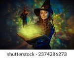 Small photo of A curly-haired young witch in a black hat and black dress conjures with a magic book of spells. Wonderful world of magic. Halloween. Magical background.