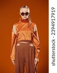 Small photo of Fashion model girl posing in stylish diamond-shaped glasses and an orange top on an orange studio background. Fashion and style for sunglasses. Summer haute couture collection.