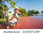 asian child or kid girl playing skateboard or surf skate in skating track and extreme sports exercise by crouching to turn hand touch floor to wearing helmet elbow knee support for body safety protect