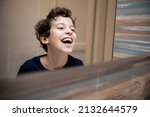 Small photo of Little boy having a spontaneous smile with open mouth watching his reflection on the bathroom mirror