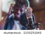 condenser microphone with antipop in front of the blurred face of an African guy singing or talking live - technology concept of young people creating contents and casting online