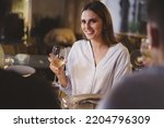 Beautiful young lady carefree enjoying a glass of white wine in an elegant restaurant on a weekend night sitting at a table with her friends - people, alcohol, lifestyle concept