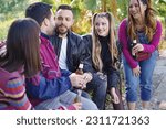 Small photo of Youthful Camaraderie and Lighthearted Fun in a Park. Group of fashionable young adults enjoying playful banter and sharing drinks outdoors.