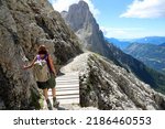 young woman crosses a wooden bridge along a stone path in the Italian Dolomites while hiking