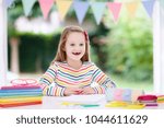 Small photo of Child doing homework for school at white desk. Little girl with school supplies, abc books, drawing and painting tools and materials. Happy back to school student. Kid learning alphabet letters